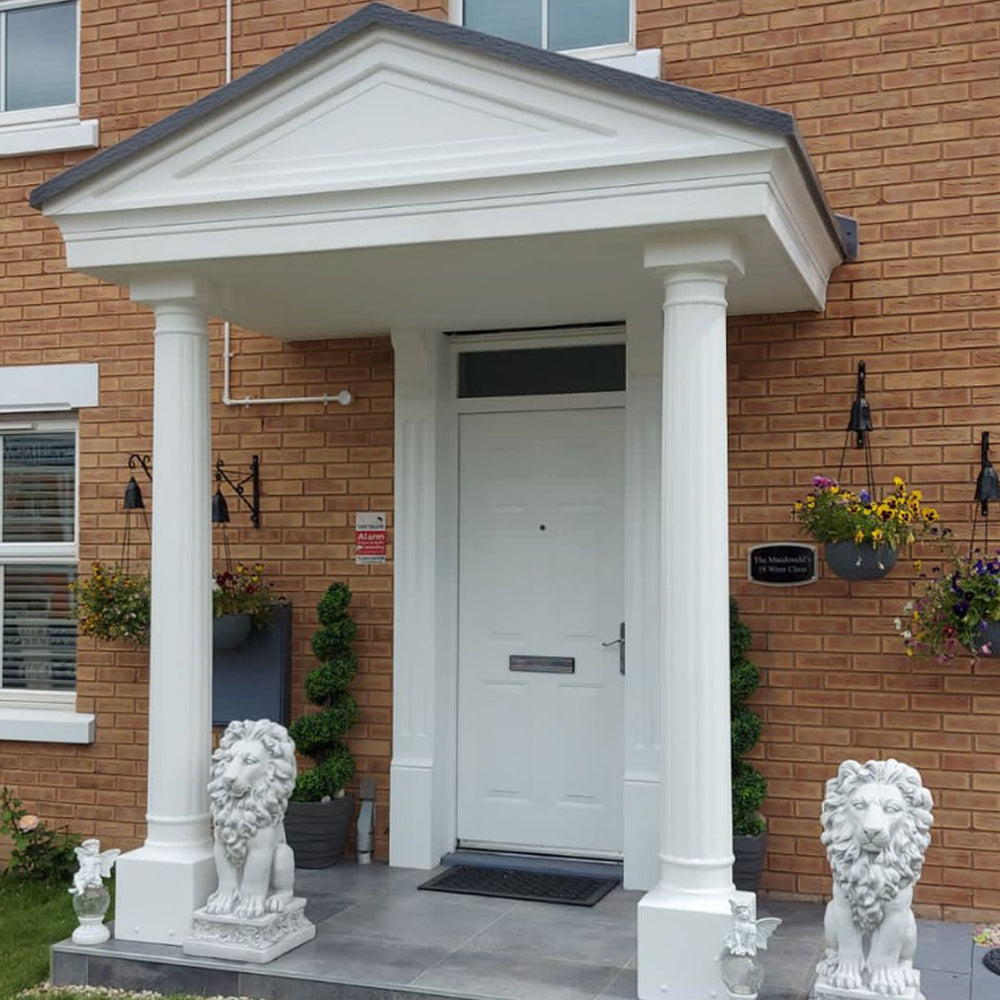 White door with portico and fluted columns and lion statues in front of a brick building