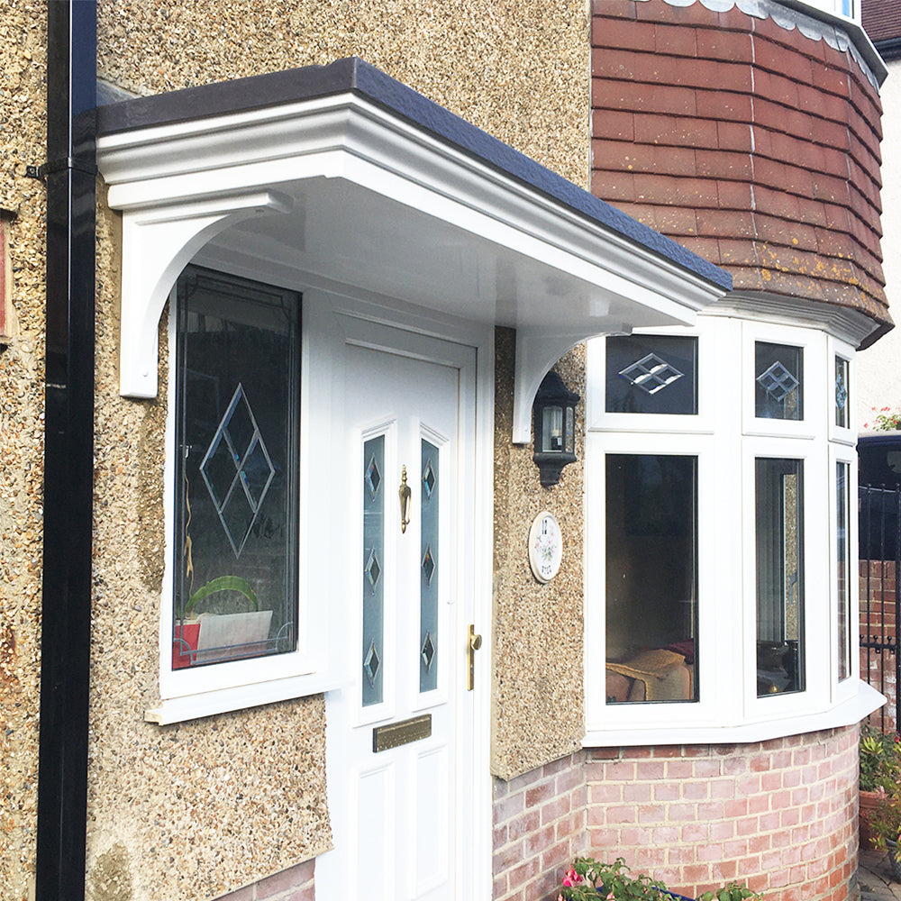 White front door with door canopy above set on a textured beige house exterior with brick detailing.