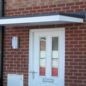 White front door with glass panels on a brick wall house with a cherwell flat roof canopy